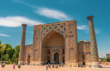 Mavi çatılı ve mavi kemerli büyük bir bina. İnsanlar binanın etrafında yürüyorlar. Avluda bir sürü insan var.