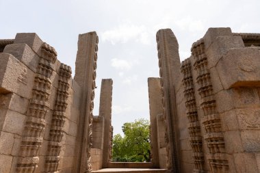 Ortasında büyük bir kemer olan büyük taştan bir bina. Kemer yolu birçok sütunla çevrili ve bina çok eski görünüyor. Gökyüzü açık ve güneş parlıyor.