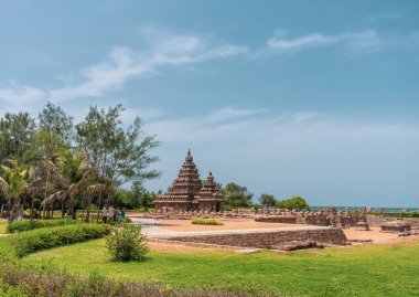 Arka planda büyük bir bina olan güzel, sakin bir tapınak manzarası. Gökyüzü açık ve mavi, çimenler gür ve yeşil. Atmosfer huzurlu ve rahatlatıcı.