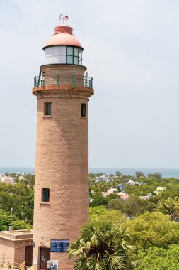 Kırmızı tepeli uzun bir deniz feneri bir su kütlesine bakan bir tepede oturur. Deniz feneri ağaçlar ve evlerle çevrili, manzaraya huzurlu ve huzurlu bir atmosfer veriyor.