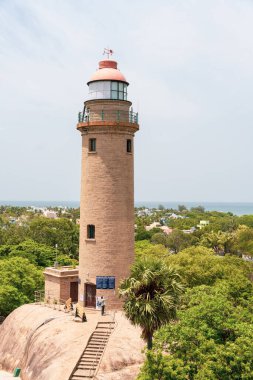 Okyanusa bakan bir tepede uzun bir deniz feneri var. Deniz feneri ağaçlarla çevrili ve birkaç kişi etrafında yürüyor. Sahne huzurlu ve sakin, deniz feneri dik duruyor.