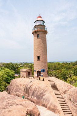 Uzun bir deniz feneri kayalık bir tepede. Deniz feneri ağaçlarla çevrili ve ona giden bir merdiveni var. Deniz fenerinin tepesinden manzara nefes kesici.