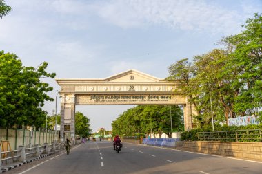 Chennai, Tamil Nadu, Hindistan - 02.07.2025: Bir adam sokakta motosiklet sürüyor. Sokak ağaçlarla kaplı ve büyük bir kemer yolu var. Chennai 'de.