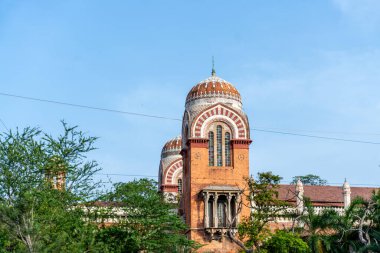 Chennai, Tamil Nadu, Hindistan - 02.07.2025: Kırmızı çatılı ve iki kubbeli büyük bir bina. Bina ağaçlarla çevrili. Gökyüzü mavi. Chennai 'de.