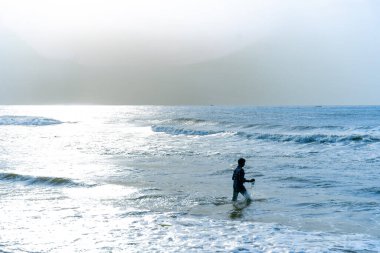 Chennai, Tamil Nadu, Hindistan - 02.07.2025: Okyanusta bir adam yürüyor. Su mavi ve gökyüzü bulutlu. Chennai 'de.
