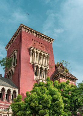 Chennai, Tamil Nadu, Hindistan - 02.07.2025: Önünde yeşil ağaç olan kırmızı bir bina. Binanın bir sürü penceresi var. Chennai 'de.