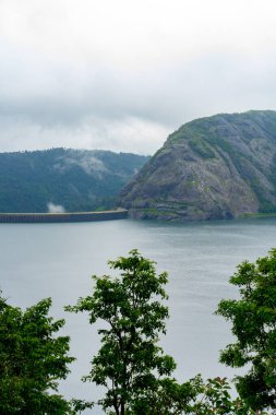 Arkasında göl olan bir dağ sırası. Gökyüzü bulutlu ve su sakin.