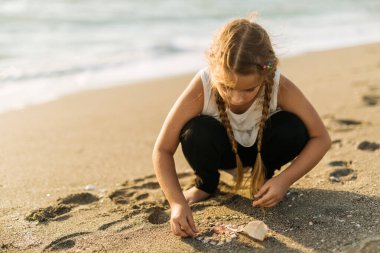 Kumsalda kumla ve deniz kabuklarıyla oynayan bir kız. Yüksek kalite fotoğraf