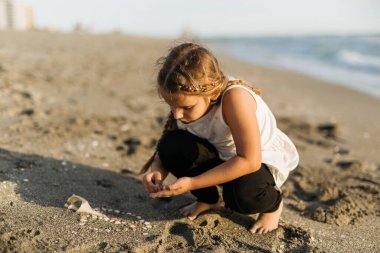 Kumsalda kumla ve deniz kabuklarıyla oynayan bir kız. Yüksek kalite fotoğraf