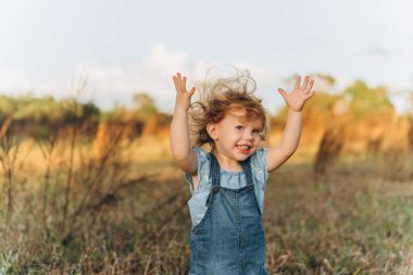 Cute red head 2 years old smiling girl with hands raised up on grassy field on sunset . High quality photo