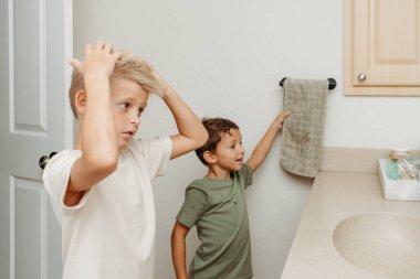 İki çocuk banyoda hazırlanıyor saçlarını tarayıp gülüyorlar. 