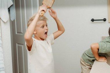 İki çocuk banyoda hazırlanıyor saçlarını tarayıp gülüyorlar. 