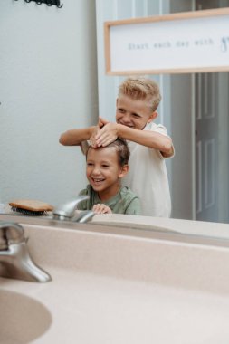 İki çocuk banyoda hazırlanıyor saçlarını tarayıp gülüyorlar. 
