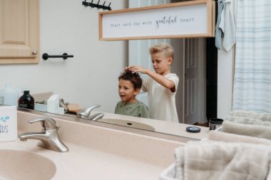 İki çocuk banyoda hazırlanıyor saçlarını tarayıp gülüyorlar. 