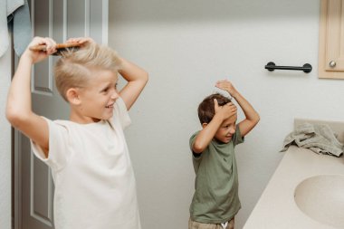İki çocuk banyoda hazırlanıyor saçlarını tarayıp gülüyorlar. 