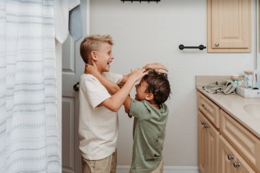 İki çocuk banyoda hazırlanıyor saçlarını tarayıp gülüyorlar. 