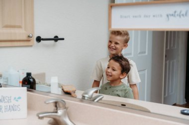 İki çocuk banyoda hazırlanıyor saçlarını tarayıp gülüyorlar. 