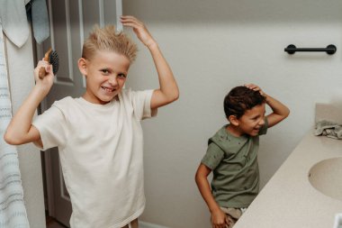İki çocuk banyoda hazırlanıyor saçlarını tarayıp gülüyorlar. 