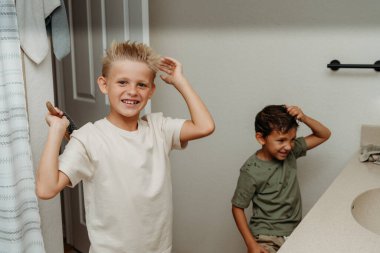 İki çocuk banyoda hazırlanıyor saçlarını tarayıp gülüyorlar. 