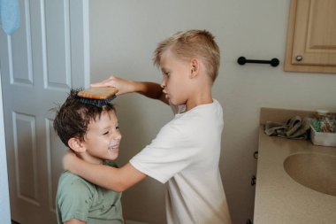 İki çocuk banyoda hazırlanıyor saçlarını tarayıp gülüyorlar. 