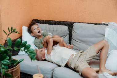 Çocuklar evin dışında oynuyorlar. Parlak güneş ışığı altında, neşeli bir atmosfer yaratıyorlar..