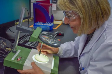 Smiling mature scientist woman wearing lab coat is counting colonies working in research laboratory for the diagnostic and analysis of diseases happy to find a health treatment at modern work center