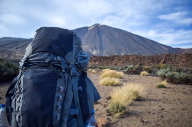 Close-up. Young traveler man hiking in the mountain towards the Teide volcano through the desert with backpack. Enjoying hot weather, sun. North Europeans on holidays in Spain. Beautiful landscape.