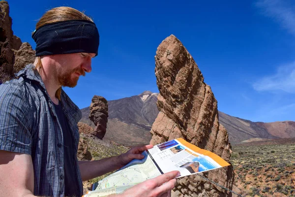 Young Handsome Tourist Mountain Hiking in the Nature. Male Adventurer Backpacker Navigating with a Map on Teide National Park in Tenerife, Canary Islands. Ginger north european wearing a bandana