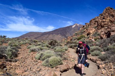 Pretty young traveler backpacker woman smiling hiking on National Park with Teide volcano on the background. Enjoying hot weather and sun in Spain. Active holiday in canary island.