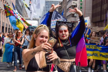 Berlin, Almanya - 23 Temmuz 2023: Christopher Street Day Berlin. Gay Gururu, Gurur Yürüyüşü. Gösteride selfie çeken iki kadın. LGBTQ + bayrağı olan insanlar ve protesto poster / afişi