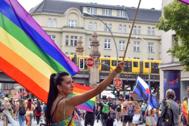 Berlin, Almanya - 23 Temmuz 2023: Christopher Street Day Berlin. Gay Gururu, Gurur Yürüyüşü. Bir gösteride kadın LGBTQ + bayrağı tutuyor. Sarı metro ve arka planda yüzüyor. Berlin U-bahn.