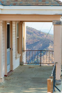 Beyaz saray verandasında, gölgede ve çimentoyla kaplı, dağlara tepeden bakan kanyon, yeşillik ve gökyüzü arka planı güneşte.