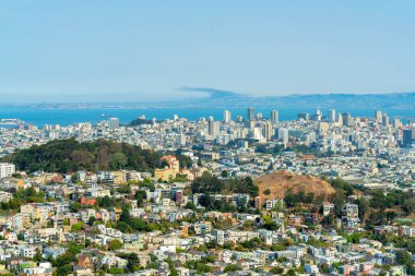 San Francisco şehir merkezinde tepeler, ağaçlar ve güneş altında ağaçlar ve ağaçlar. Evleri ve komşuları var. Arka planda okyanus ve mavi ve beyaz gökyüzü var.