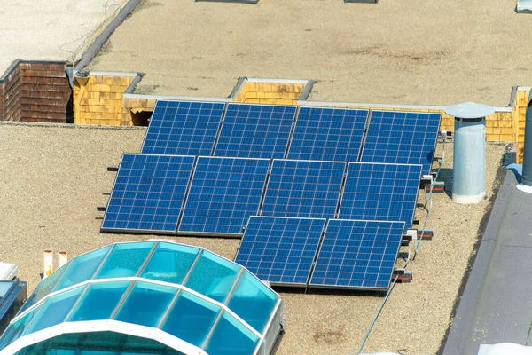 Sunlit black solar panels on flat gravel rooftop midday. Aerial shot of urban rooftop in city or in neighborhood late afternoon.