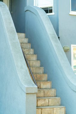 Evin ön bahçesinde, pencereli ön bahçesinde mavi tırabzanlar olan bej renkli fayans merdivenler öğleden sonra gölgede kalıyor. Banliyö ortamında binaya giriş.