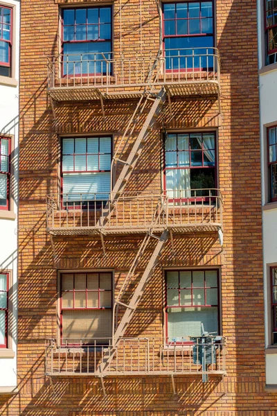 Brick building with fire saftey escape ladder with windows in sun and shade in mid afternoon sun in the city downtown. Urban setting with open shade in apartment in the city and neighborhood.