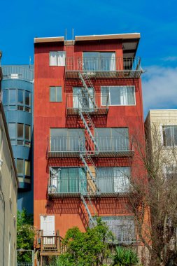 Mahallede öğle güneşinde mavi ve bej binaları olan kırmızı sıva ev ve çok sayıda pencere ve balkon bulunuyor. Şehirde ya da kenar mahallelerde ya da mavi gökyüzü arka planlı kentlerde..