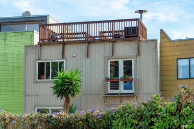 Çatı terası ya da balkonları olan renkli evler. Hepsi de ahşap çerçeveli ahşap korkuluklar ve eğlence için ısıtıcılar. Gölgede yeşil ve bej binalar, mavi ve beyaz gökyüzü arkaplanı.