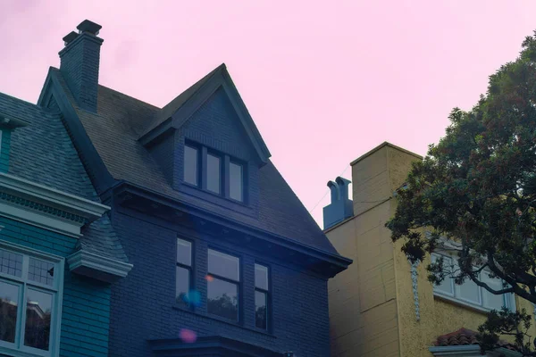 Uğursuz, mor günbatımı gökyüzü San Francisco California 'da akşam güneşinde karanlık Victoria evlerinin üzerinde beliriyor. Mahallede ve ön bahçe ağaçlarında gri ve bej renkli evler var..