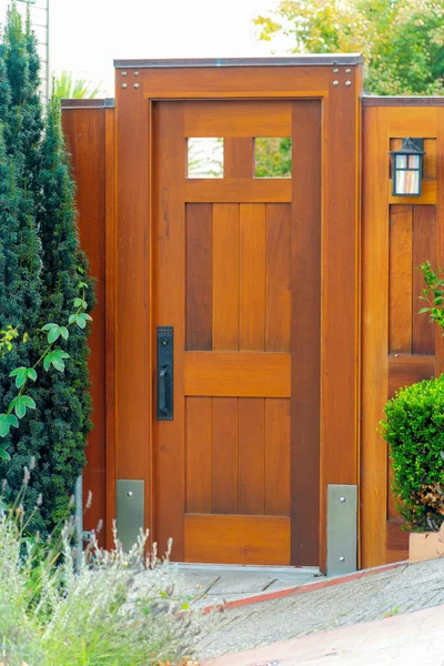 Kahverengi ahşap ve modern güvenlik kapısı. Metal donanım ve ağaçlar ön bahçemizde çalı çırpıyor. Öğleden sonra güneş ışığı altında özel hayat ve güvenlik ihlali önlemek için..