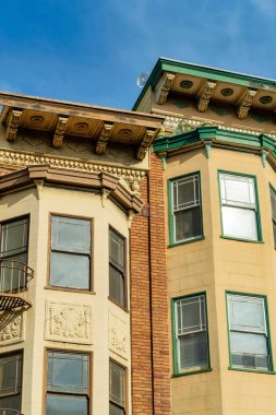 Düz çatılı ve dekoratif boyalı modern kahverengi taş binanın yan tarafında iki dış pencere kulesi var. Gün ortası güneşinde mavi gökyüzü arka planında mahallede ya da şehrin kentsel bir bölgesinde.