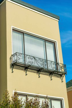 Çiçekler için dekoratif balkon, mavi gökyüzü arka planında koyu pencere ve çatı aksanı olan kremalı ya da bej renkli ev cephesi. Öğleden sonra bir banliyö bölgesinde ya da mahallede güneş batarken.