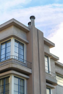 Uzun bacalı ev cephesi güzel dekoratif pencereler ve öğleden sonra gölgesinde bej bir sıva. Beyaz bulutlu mavi gökyüzü mahallede ya da banliyö şehrinde.