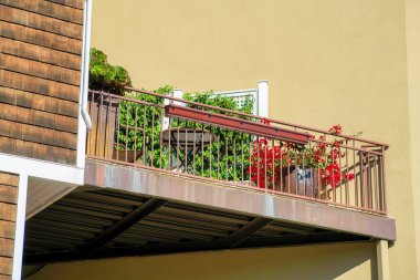 Köşedeki kama, mahalledeki balkon ve terasta ya da evin yan tarafındaki banliyö ortamında parçalanmış. Balkonda sıva duvarlı bitkiler ve şehir merkezindeki binada ahşap panellerle..