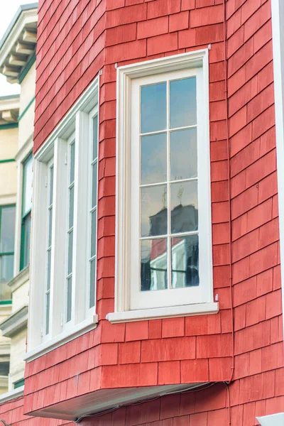 Bay window on cubby in side of red slatted wood building with white accent paint around glass windows in the neighborhood. In afternoon sun in the city or in a suburban part of the downtown.