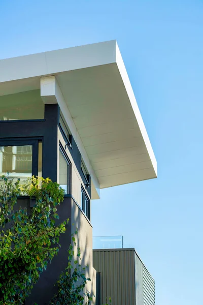 stock image Decorative building facade with modern white roof extending over the house in late afternoon sun and front yard trees. In the neighborhood or in the city with blue house and sky background.