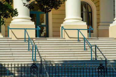 Büyük panoramik merdivenler çimento basamakları ve gri metal el rayları ile dekoratif Amerikan sütunları ile siyah güvenlik kapısı ile girişte. Şehir merkezinin kentsel kesiminde öğleden sonra güneşinde.