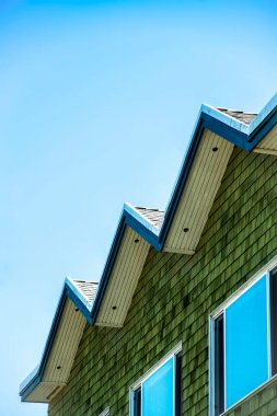 Zig zag çatısı, mavi ve beyaz boyalı kahverengi ahşap ya da ahşap kaplamalı ve mavi gökyüzü açık arka planda gölgede. Binanın, evin ya da evin dış tarafında görülebilir yansıtıcı pencereler.