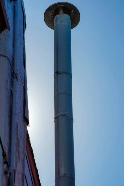 stock image Close view of gray metal chimney pipes in sunset or twilight sun on side of building with wooden facade and blue sky background. In the city or in an urban area of the town downtown.