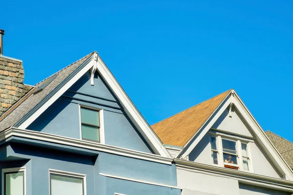 stock image Row of modern roofs on two seperate houses one white and blue with orange roof tiles and double gable with visible chimney. In blue sky background with no clouds in midday sun in neighborhood.